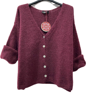 Burgundy cardigan with buttons on a hanger against a light brick wall.