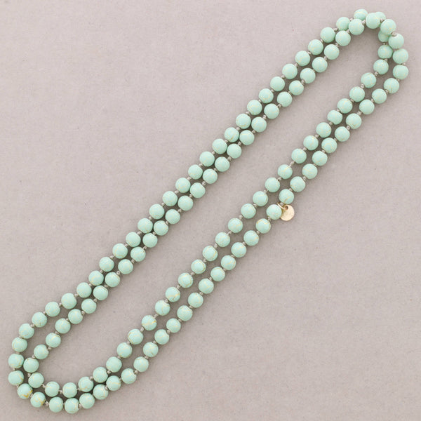 Turquoise beaded necklace on a light pink background
