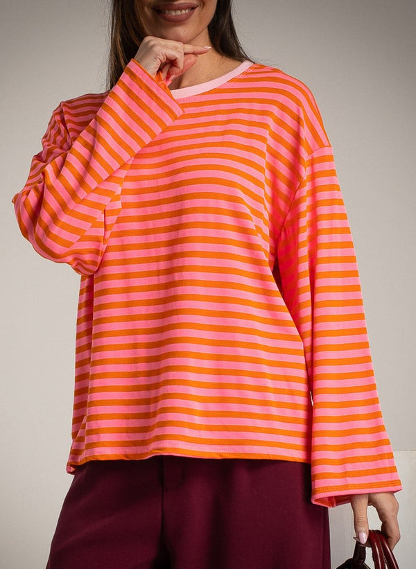 Person wearing a pink and orange striped long-sleeve top with burgundy pants against a neutral background