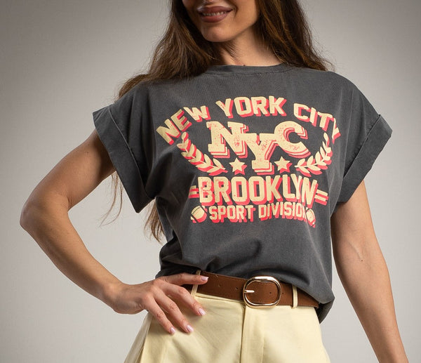 Person wearing a dark gray t-shirt with 'New York City Brooklyn Sport Division' print, paired with light-colored pants.