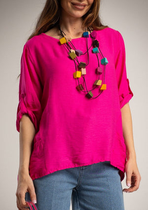 Woman wearing a bright pink top and blue jeans with a colorful necklace against a neutral background
