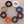 Load image into Gallery viewer, Eight beaded bracelets arranged in a circle on a neutral taupe background, showing different bead colors: black, white, blue, maroon, dark brown, orange, gold, and dark green.
