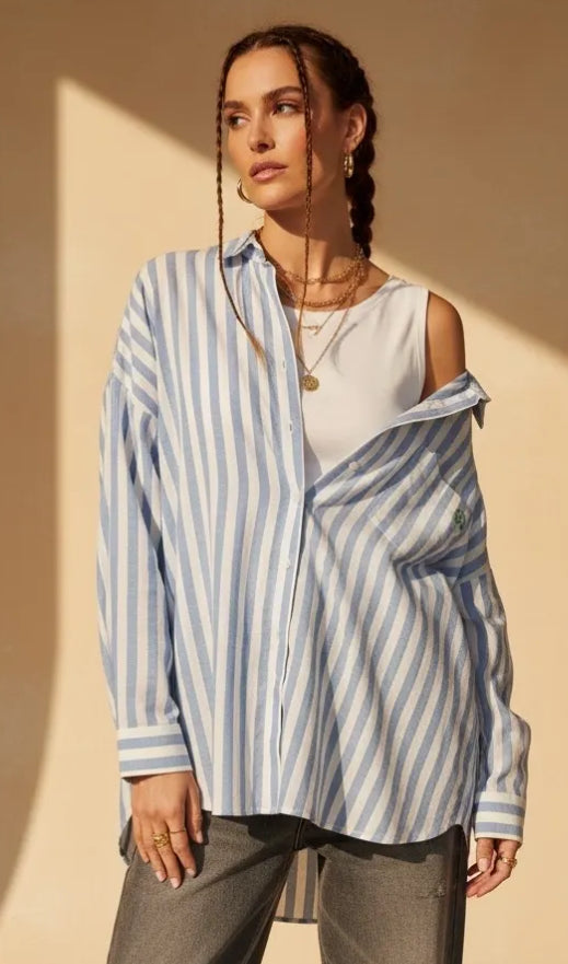 Woman wearing a blue and white striped shirt over a white top with a beige background