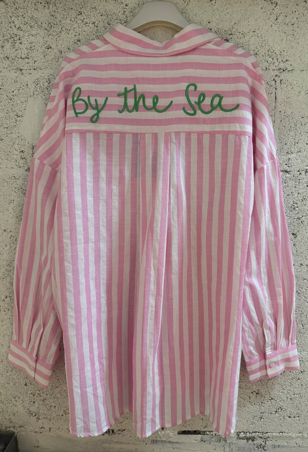 Pink and white striped shirt with 'By the Sea' text on a textured wall background
