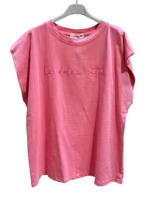 Pink t-shirt with 'la dolce vita' text on a hanger against a plain background