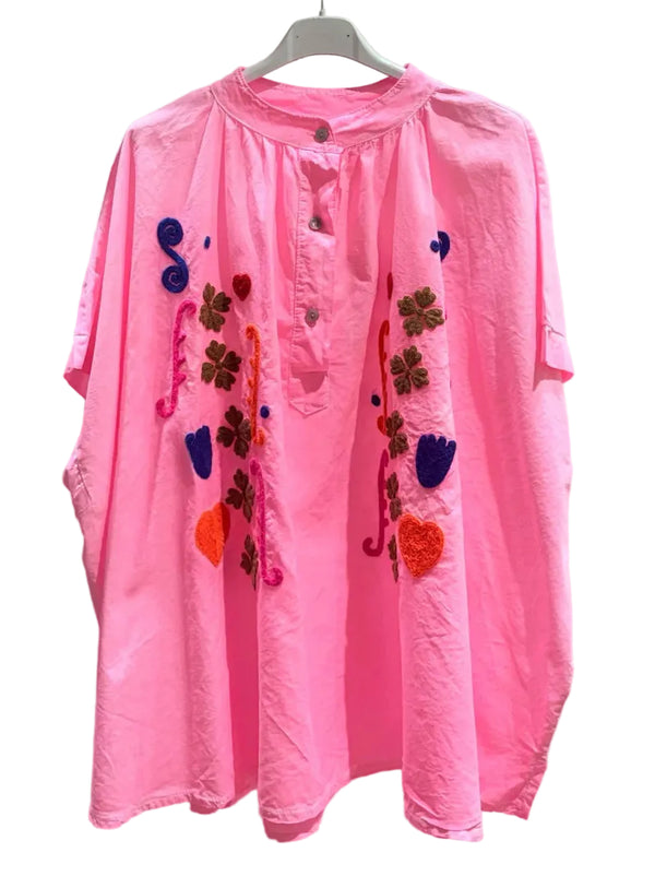 Pink shirt with colorful embroidered designs on a white background