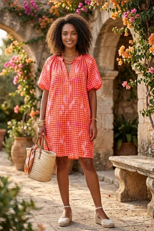 Woman in a red checkered dress standing in a decorative outdoor setting with flowers and stone arches.