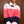 Load image into Gallery viewer, A woman seated indoors wearing a fuzzy color-block cardigan with pink, coral-red, and dark purple horizontal sections, layered over a white collared shirt and dark trousers.
