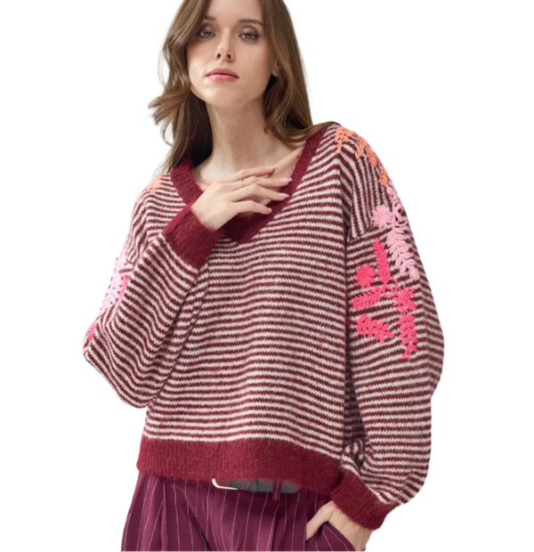 Woman wearing a maroon and pink striped sweater with an embroidered sleeve details on a white background
