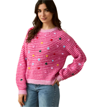 Woman wearing a pink sweater with colorful hearts against a beige background