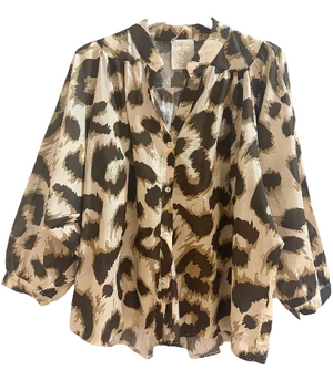A long-sleeve button-up blouse with a beige, brown, and black leopard print pattern, hanging on a white hanger against a textured light gray wall.