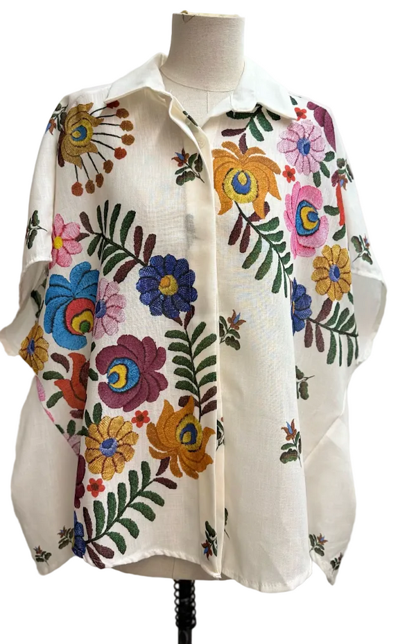 A cream-colored short-sleeve button-up shirt with a vibrant multicolor floral and leaf pattern, displayed on a mannequin torso against a plain light gray background.