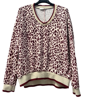 A women's long-sleeve knit sweater with a leopard print pattern in burgundy and cream, featuring ribbed v-neck, cuffs, and hem with matching burgundy and cream trim, hanging on a black hanger against a white brick wall.