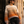 Load image into Gallery viewer, A woman wearing a chunky knit sweater with horizontal stripes in cream, beige, tan, orange, and mauve, paired with dark jeans and sunglasses, leaning against a black wrought-iron gate and beige stone building.
