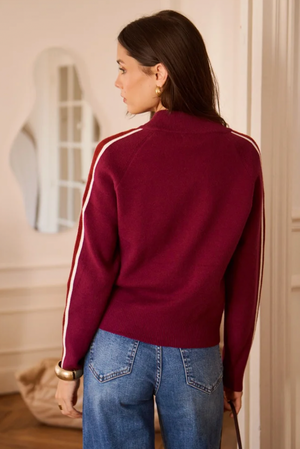 Back view of a woman wearing a women's burgundy fine-knit mock-neck zip-up cardigan with white contrast racing stripes down the sleeves, styled with blue high-waisted jeans.