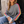 Load image into Gallery viewer, A woman sitting outdoors in front of a dark doorway wearing a gray knit sweater with bright rainbow stripes running down the sleeves, paired with light blue jeans and holding a white coffee cup.
