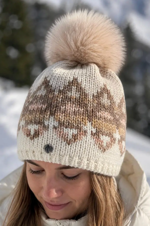 "Woman wearing a white and beige Fair Isle knit beanie with a fluffy pom pom in the snow" 