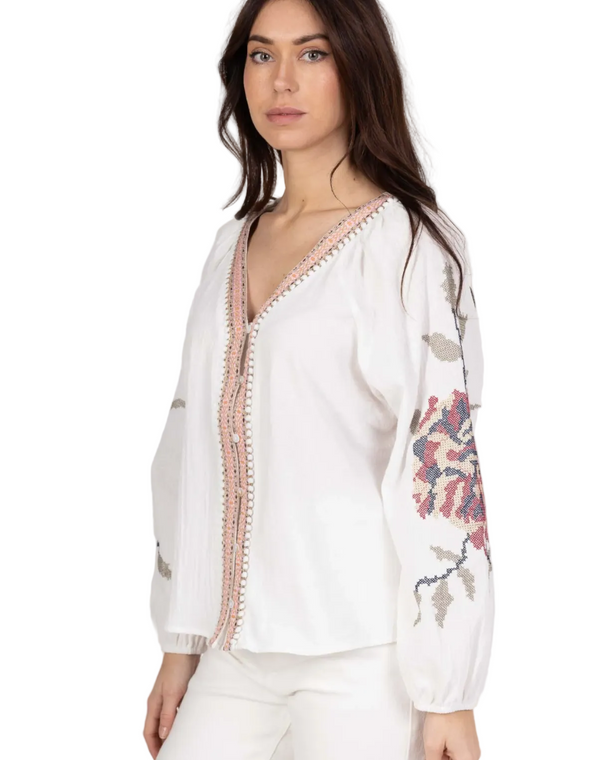 Woman wearing a white blouse with floral embroidery on a plain background