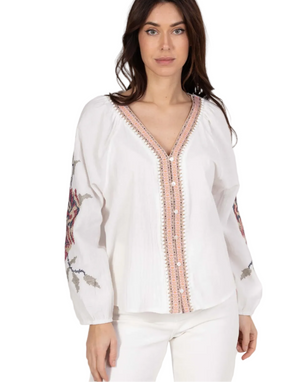 Woman wearing a white blouse with floral embroidery on a plain background