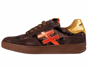 Another Trend sneaker in dark brown suede with a metallic gold heel tab, brown laces, a brown rubber sole, and a prominent orange-red embroidered cross logo on the side.