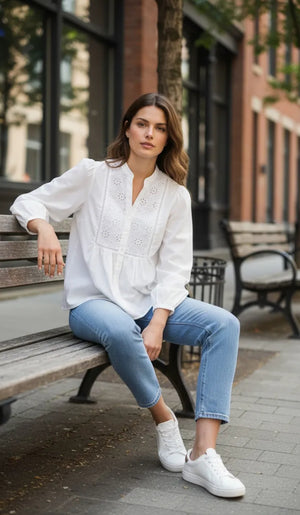 Woman sitting on a bench wearing a white blouse and blue jeans in an urban setting.
