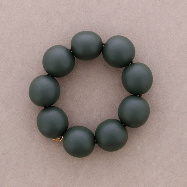 A beaded bracelet made of matte dark green round beads, arranged in a circle on a neutral beige background.