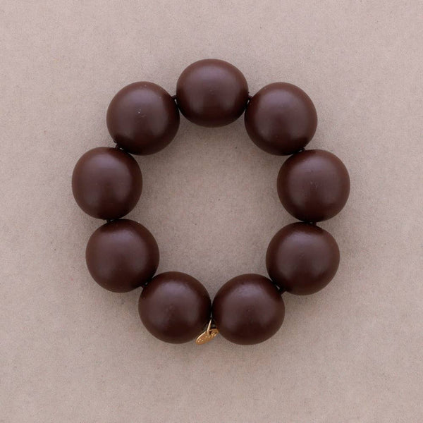 A dark brown beaded bracelet with large, smooth round beads and a small gold clasp, displayed on a neutral beige textured background.