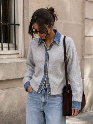 Front view of a woman wearing a grey  fine-knit button-up cardigan featuring a contrast light-wash denim collar, placket, and layered cuffs, finished with polished gold dome buttons and styled with white pants