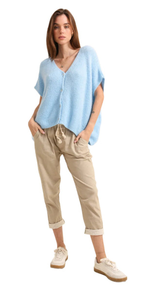 Woman wearing a light blue poncho and beige pants on a plain background